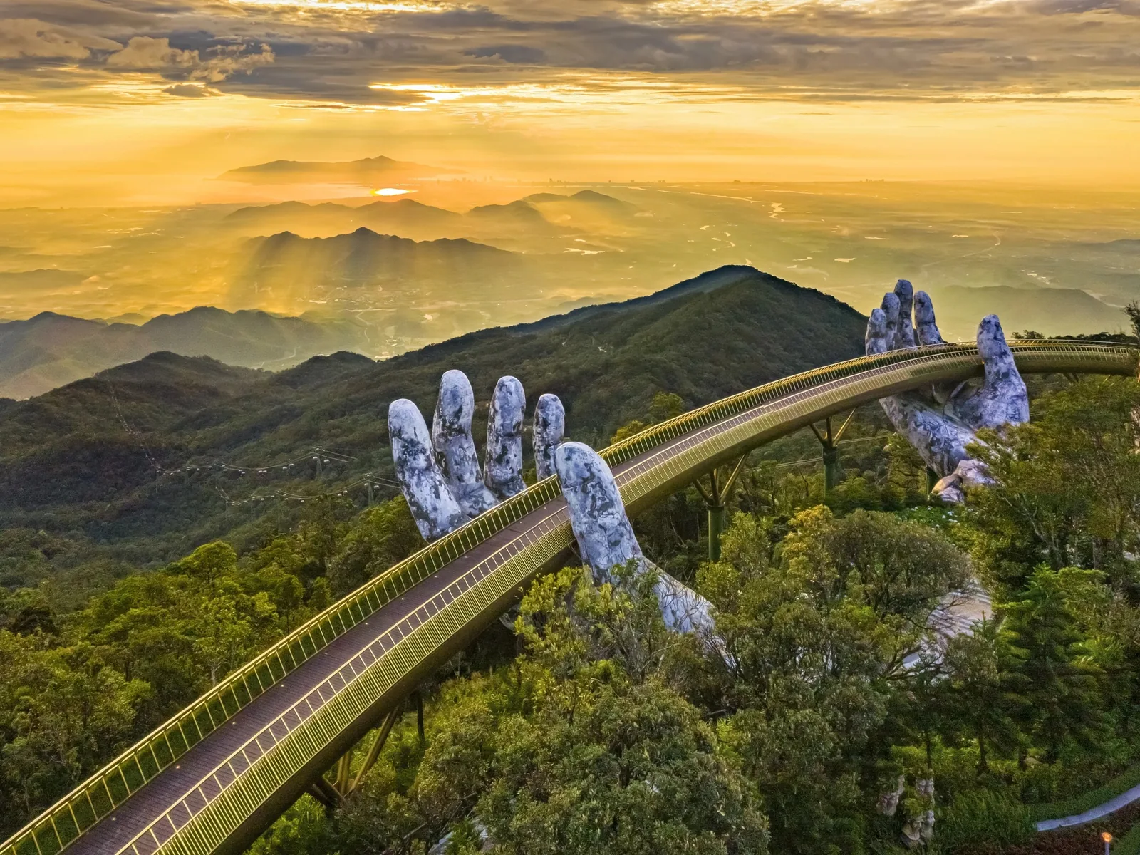 Giant stone hands appear to lift the Golden Bridge above misty mountains at sunrise at Ba Na Hills. Giant stone hands appear to lift the Golden Bridge above misty mountains at sunrise at Ba Na Hills.