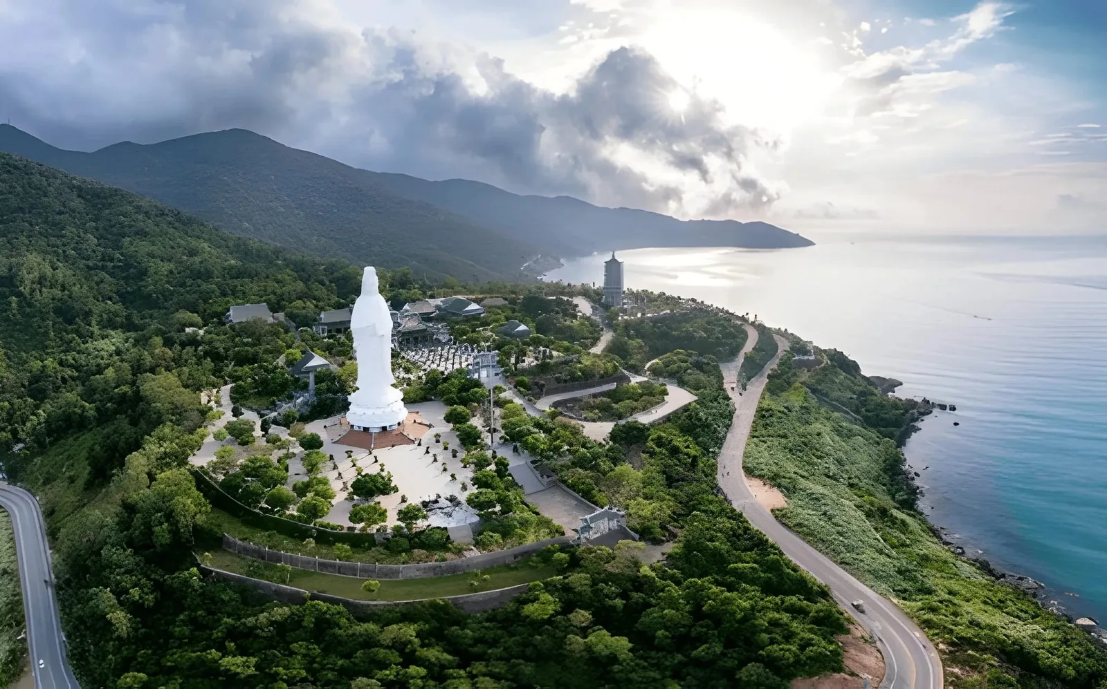 Aerial view of the tall white Lady Buddha statue at Linh Ung Pagoda overlooking Da Nang's coastline and green hills.