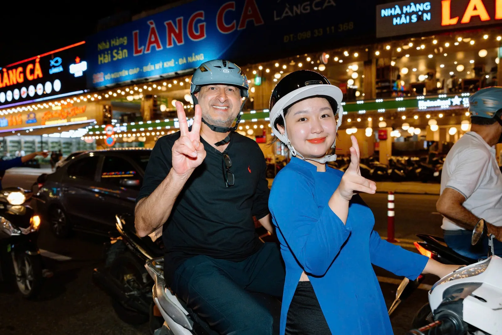 Tourists on a helmeted motorbike tour pose with peace signs on a lively night street in Da Nang. Tourists on a helmeted motorbike tour pose with peace signs on a lively night street in Da Nang.