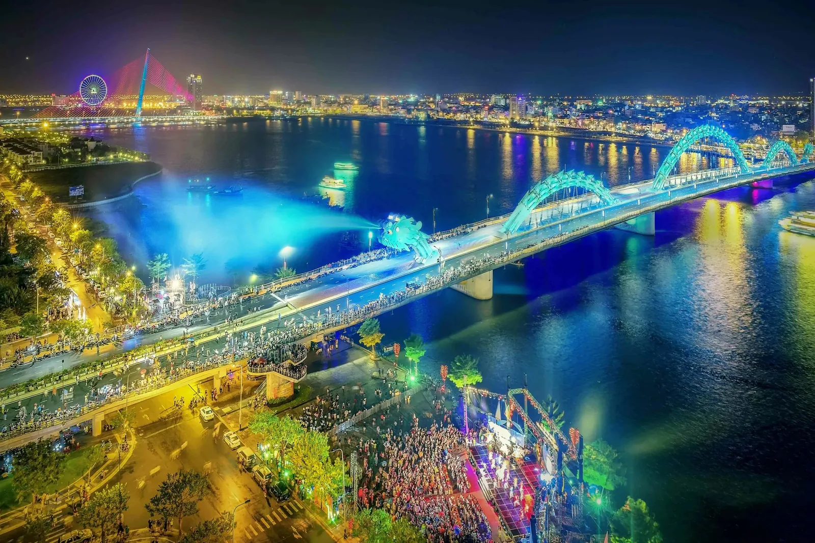 The illuminated Dragon Bridge spans the Han River in Da Nang, with crowds gathered along the riverside at night. The illuminated Dragon Bridge spans the Han River in Da Nang, with crowds gathered along the riverside at night.