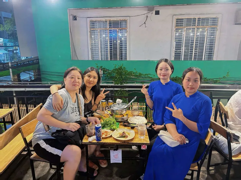 Four women pose over a hotpot dinner at an outdoor restaurant table in Da Nang at night. Four women pose over a hotpot dinner at an outdoor restaurant table in Da Nang at night.