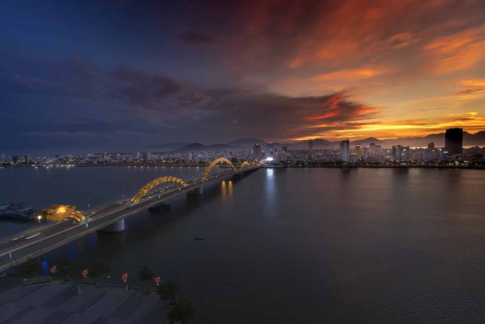 The Dragon Bridge glows over the Han River at sunset with Da Nang's skyline under a fiery sky. The Dragon Bridge glows over the Han River at sunset with Da Nang's skyline under a fiery sky.