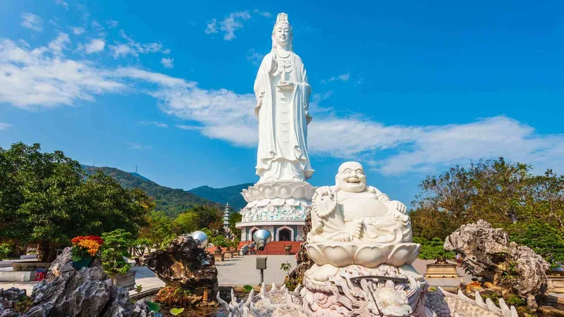 A towering white Lady Buddha statue rises above Linh Ung Pagoda in Da Nang, with a laughing Buddha figure in the foreground. A towering white Lady Buddha statue rises above Linh Ung Pagoda in Da Nang, with a laughing Buddha figure in the foreground.