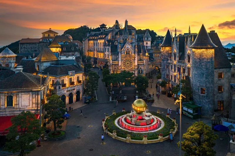 European-style castle towers and a glowing globe fountain light up at sunset in Ba Na Hills, Da Nang. European-style castle towers and a glowing globe fountain light up at sunset in Ba Na Hills, Da Nang.