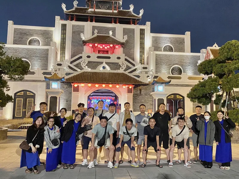 A group tour poses at night in front of an ornate illuminated temple-style building in Da Nang. A group tour poses at night in front of an ornate illuminated temple-style building in Da Nang.