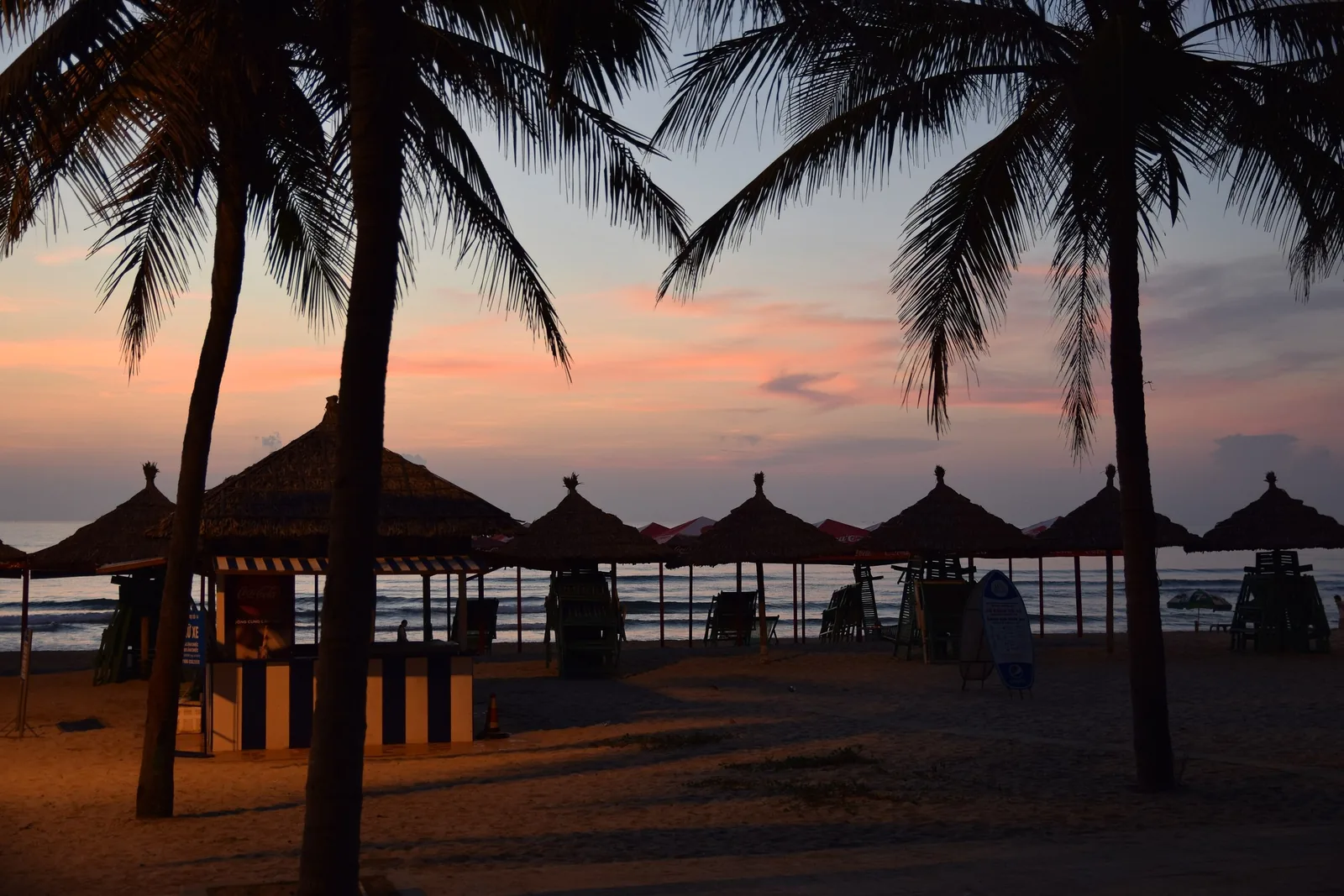 Palm trees and thatched beach umbrellas silhouetted against a colorful sunset sky on Da Nang beach. Palm trees and thatched beach umbrellas silhouetted against a colorful sunset sky on Da Nang beach.