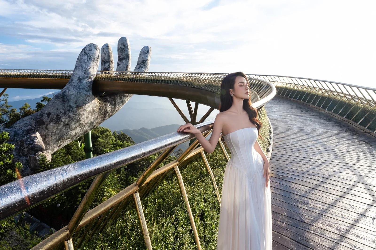 A woman in a white dress poses on the Golden Bridge beneath its giant stone hand at Ba Na Hills.