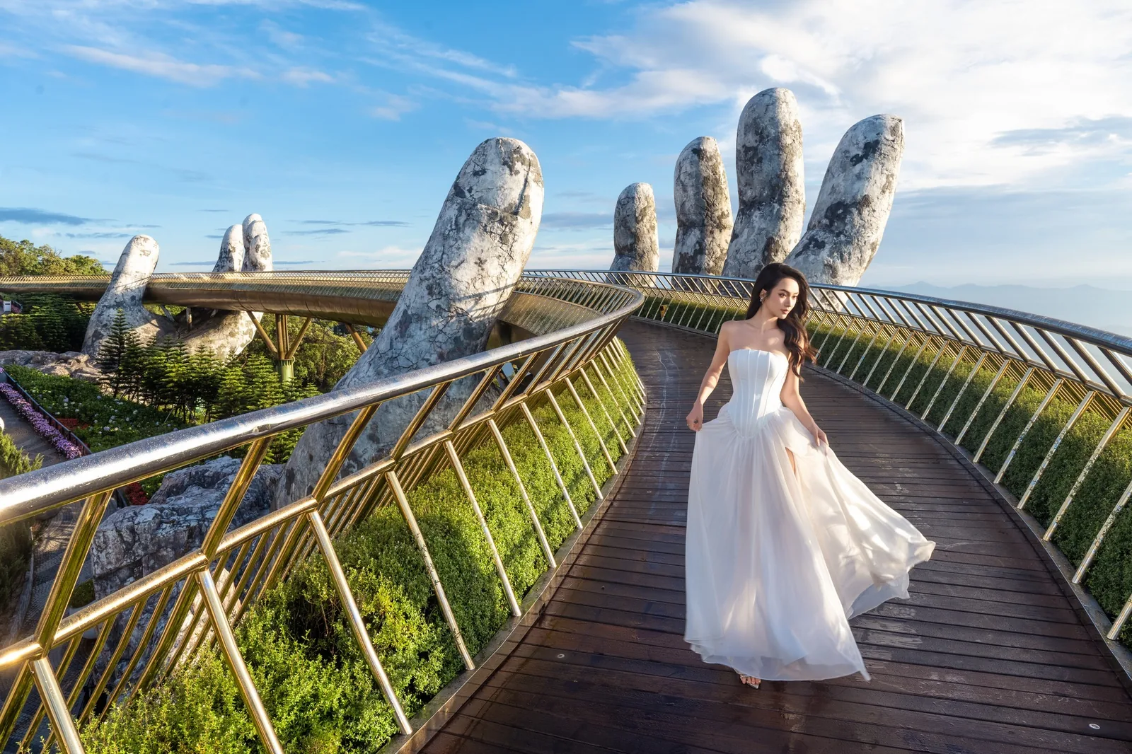 A woman in a flowing white dress walks along the Golden Bridge beneath its giant stone hand at Ba Na Hills. A woman in a flowing white dress walks along the Golden Bridge beneath its giant stone hand at Ba Na Hills.