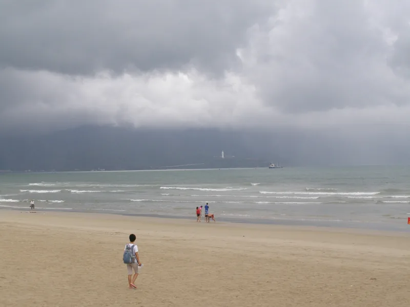 A cloudy sky looms over Da Nang beach as people walk along the sandy shore near the water. A cloudy sky looms over Da Nang beach as people walk along the sandy shore near the water.