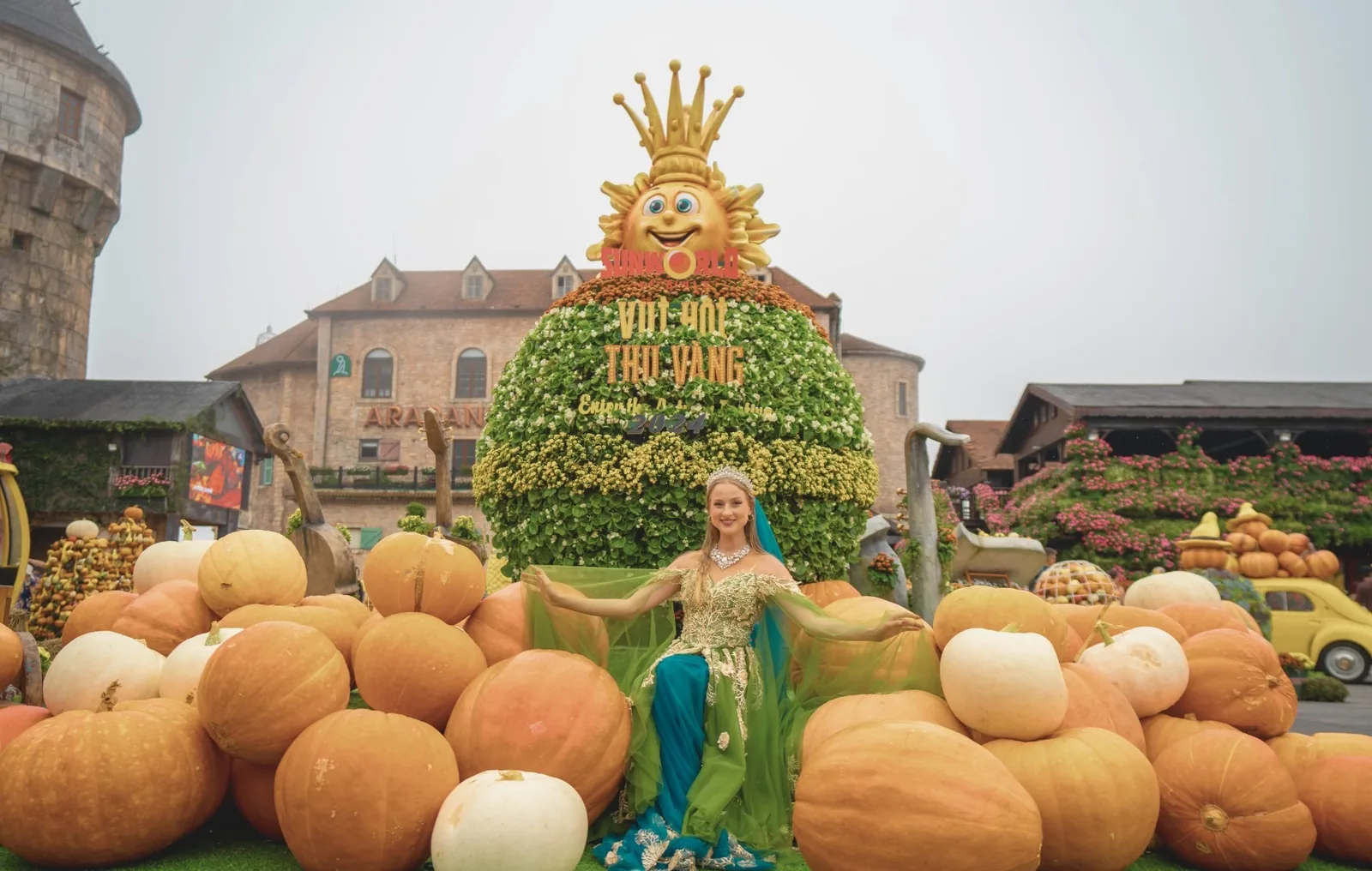 A costumed performer poses amid a pumpkin display and floral sun sculpture at Ba Na Hills. A costumed performer poses amid a pumpkin display and floral sun sculpture at Ba Na Hills.